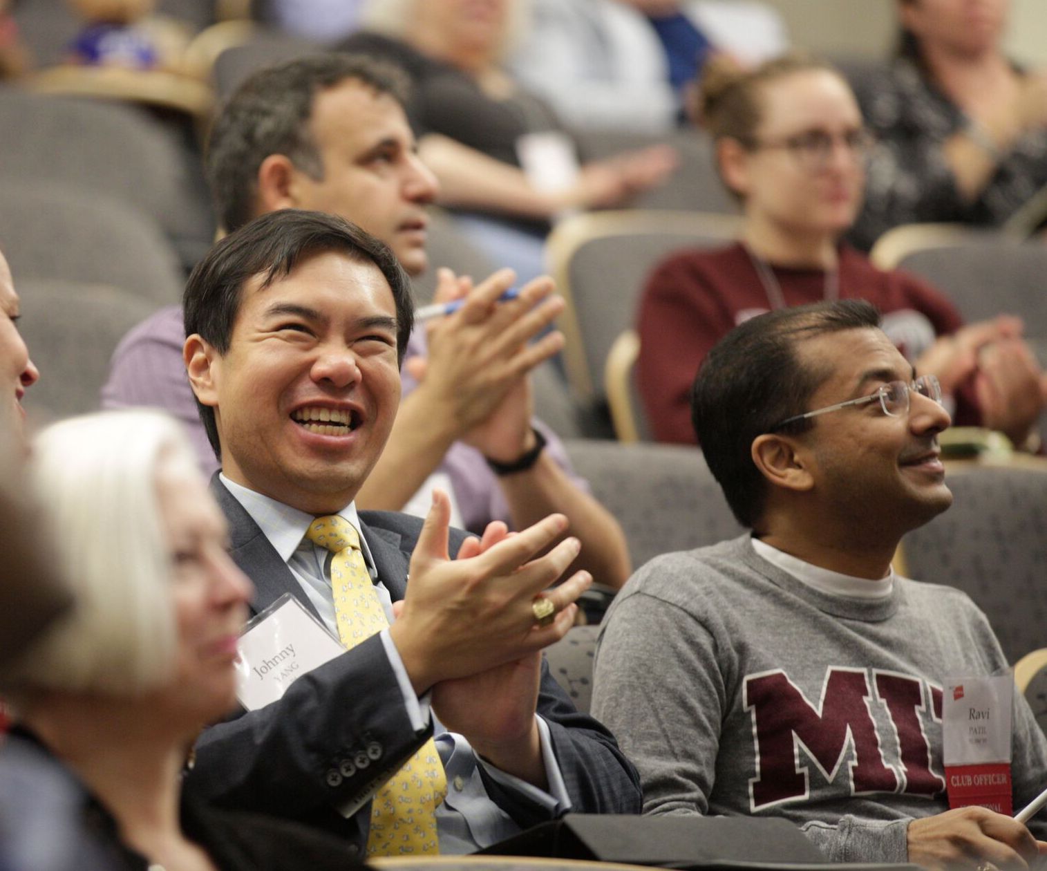 Alumni seated in an auditorium smile and clap.