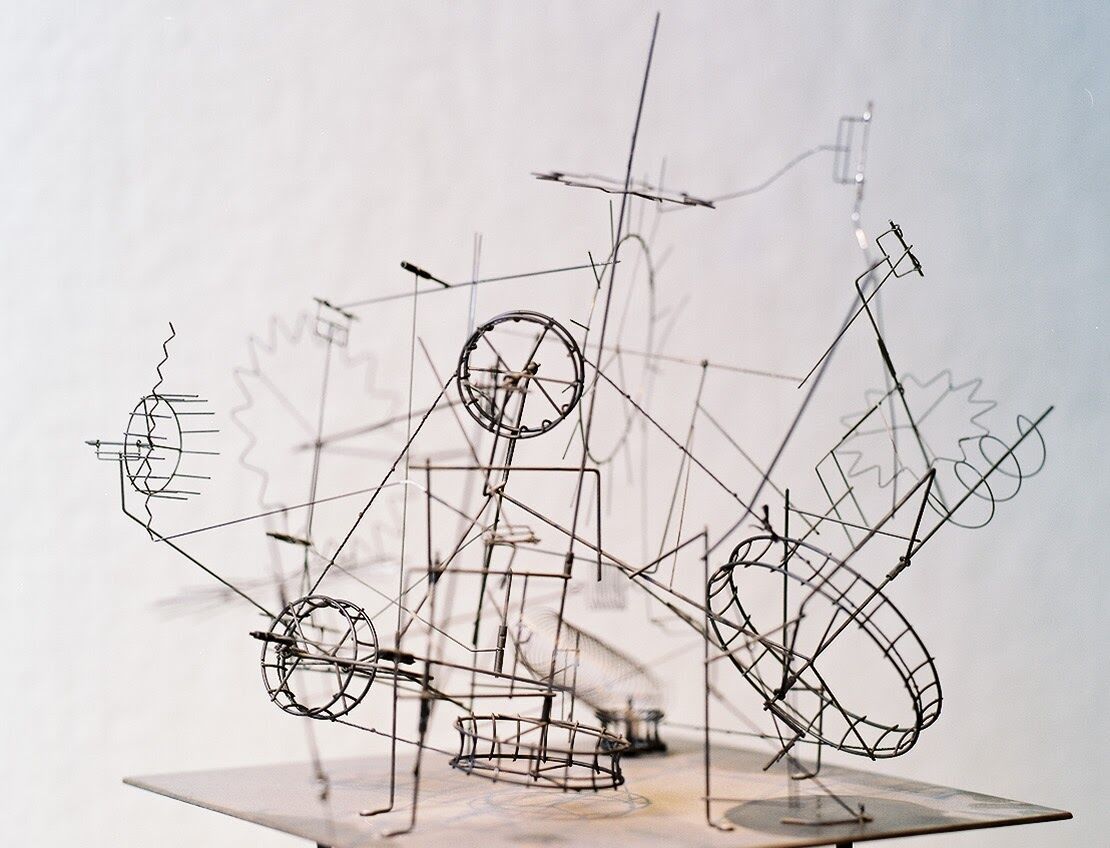 A sculpture created by Arthur Ganson composed of black wire. The shapes include circles, straight lines, and coils.