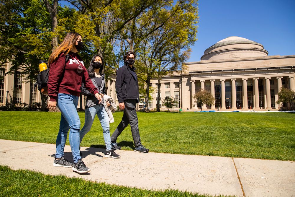 Students wearing masks walk past the Great Dome on the MIT campus.