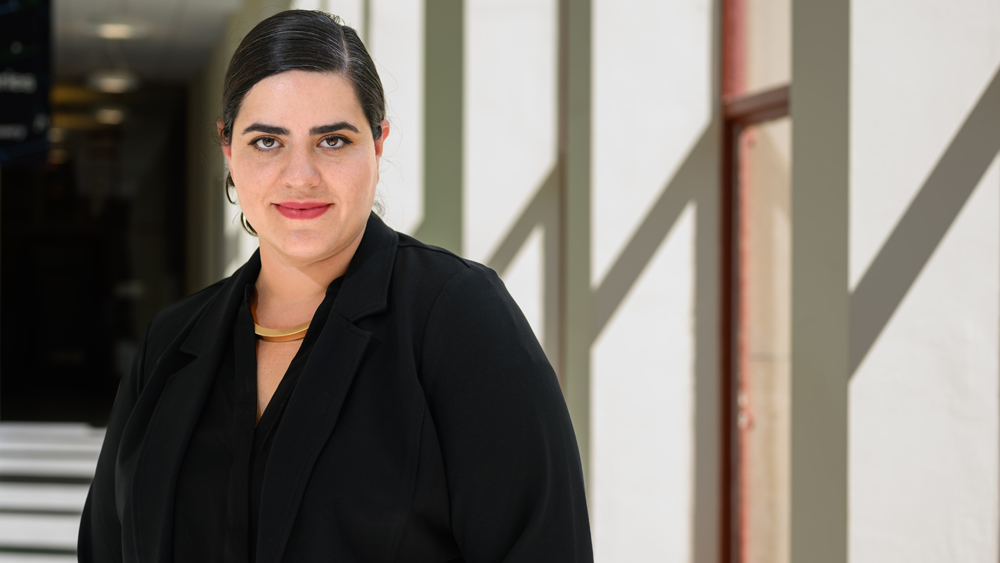 Mariel García-Montes stands in a halfway with diagonal light from windows.