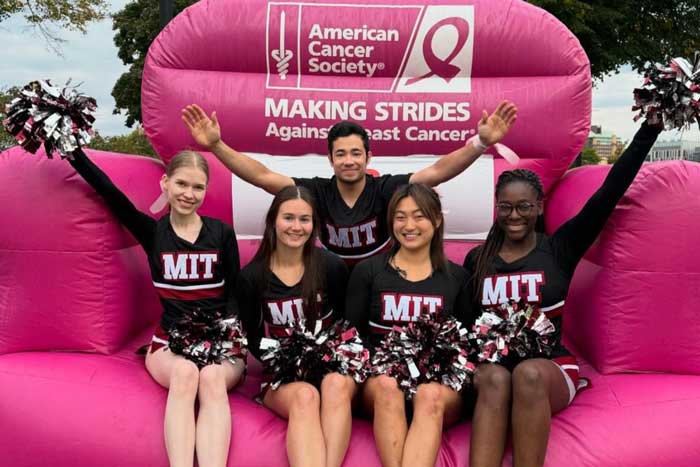 5 cheerleaders sit on a giant pink inflatable chair that says "American Cancer Society"